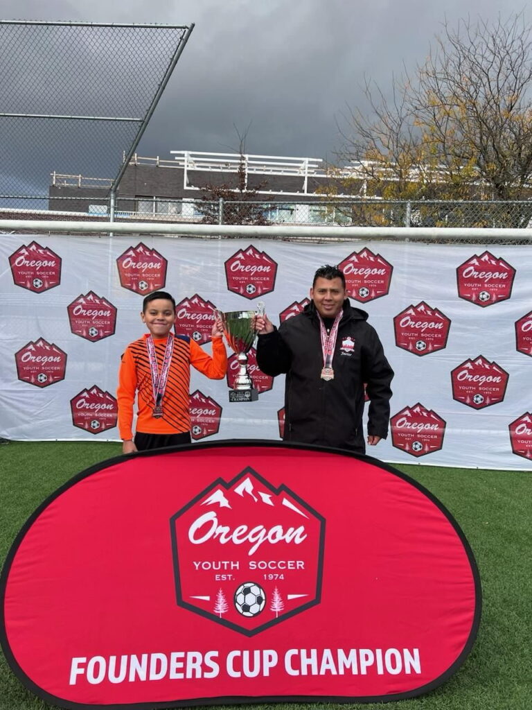 Coach Javier and player celebrating with a trophy, character development at Genesis Futbol Club, a Portland youth soccer club