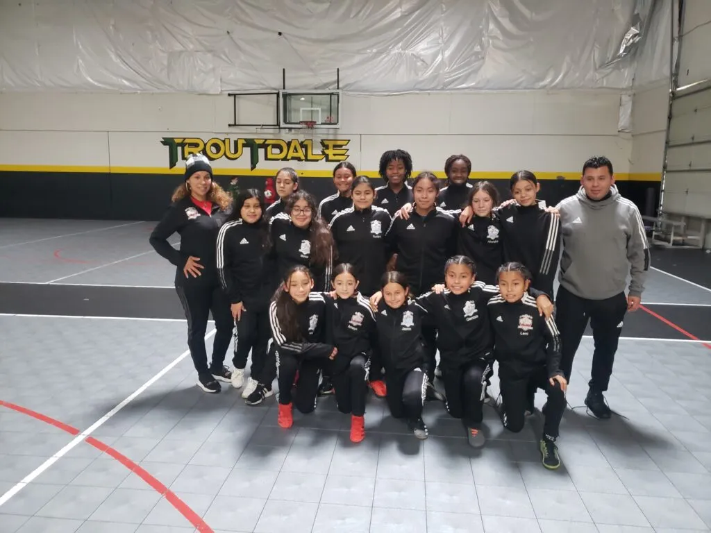 Genesis FC girls soccer team and coach posing together indoors