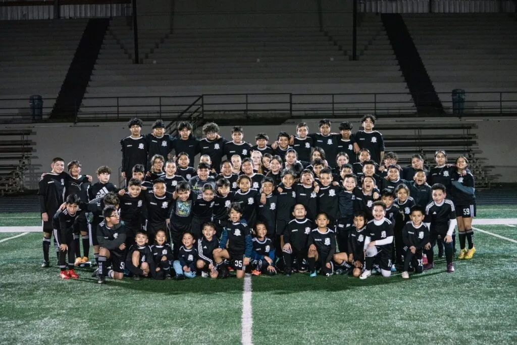 Full Genesis Futbol Club photo of youth players and coaches on the field at night