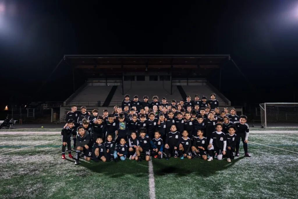 Genesis Futbol Club youth players and coaches gathered on the field under the lights
