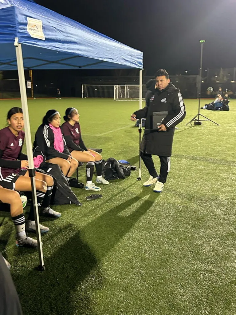 Genesis FC coach instructing seated players during a night practice